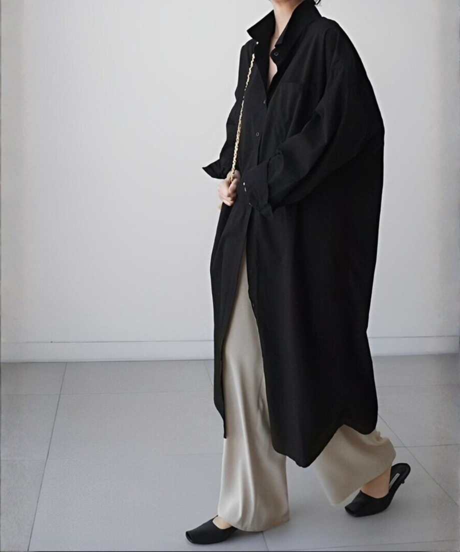 黒いロングシャツワンピースを羽織り、ベージュのワイドパンツと黒いローヒールサンダルを合わせた女性が歩いている横向き全身。