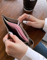 グレーのスリムな二つ折り財布を開き、中に紙幣が収納されている様子を、ネイルをした手が持っている接写写真。