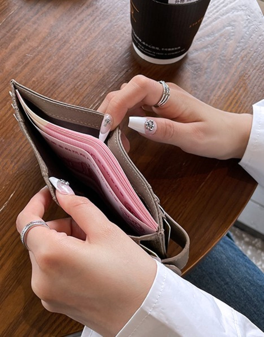 グレーのスリムな二つ折り財布を開き、中に紙幣が収納されている様子を、ネイルをした手が持っている接写写真。