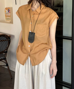 カフェのような店内で、ブラウンのシャツをルーズに着こなす女性の立ち姿。