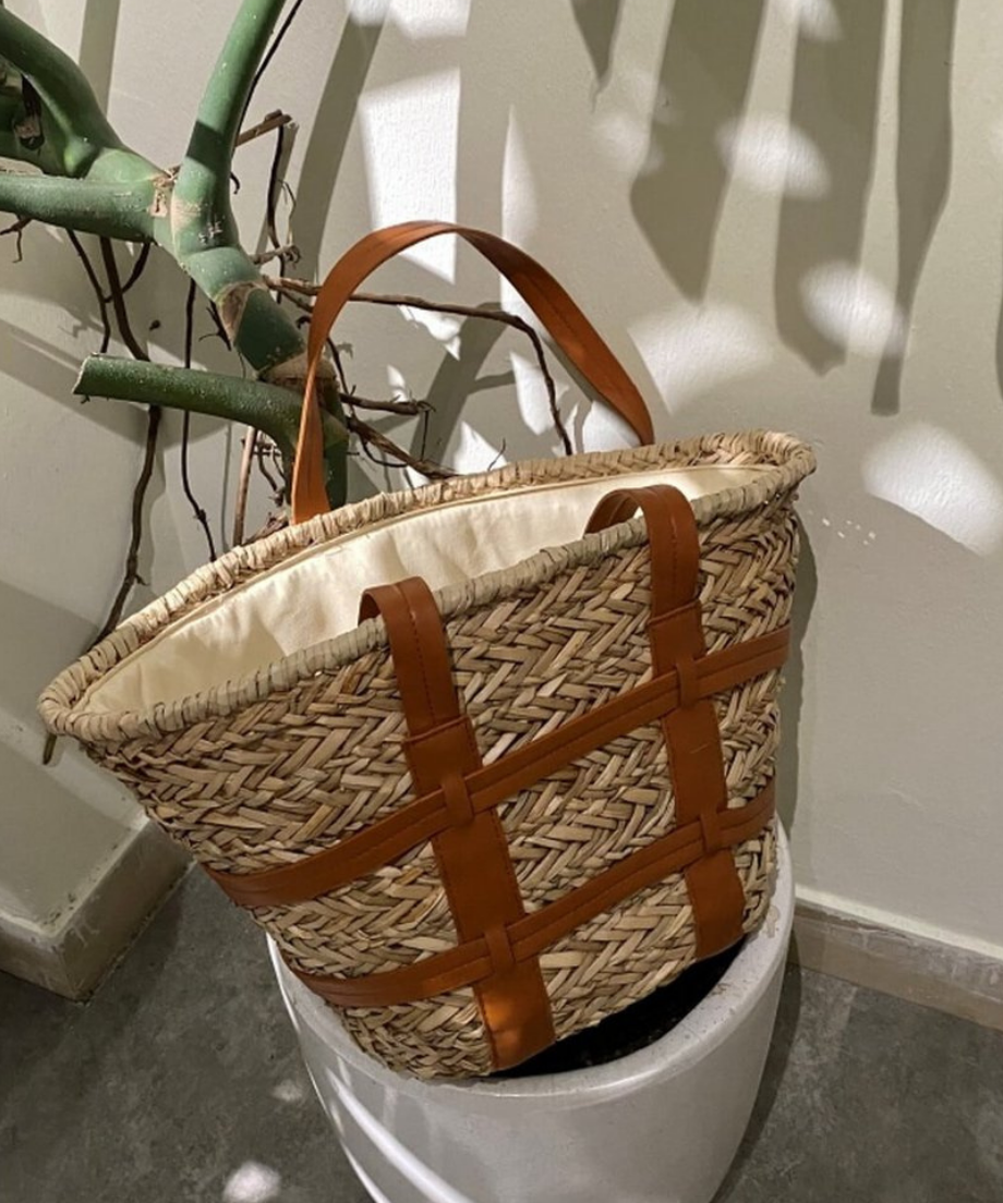 白い鉢植えの植物に立てかけられた、上品なブラウンカラーのストラップ付きストローバッグ。