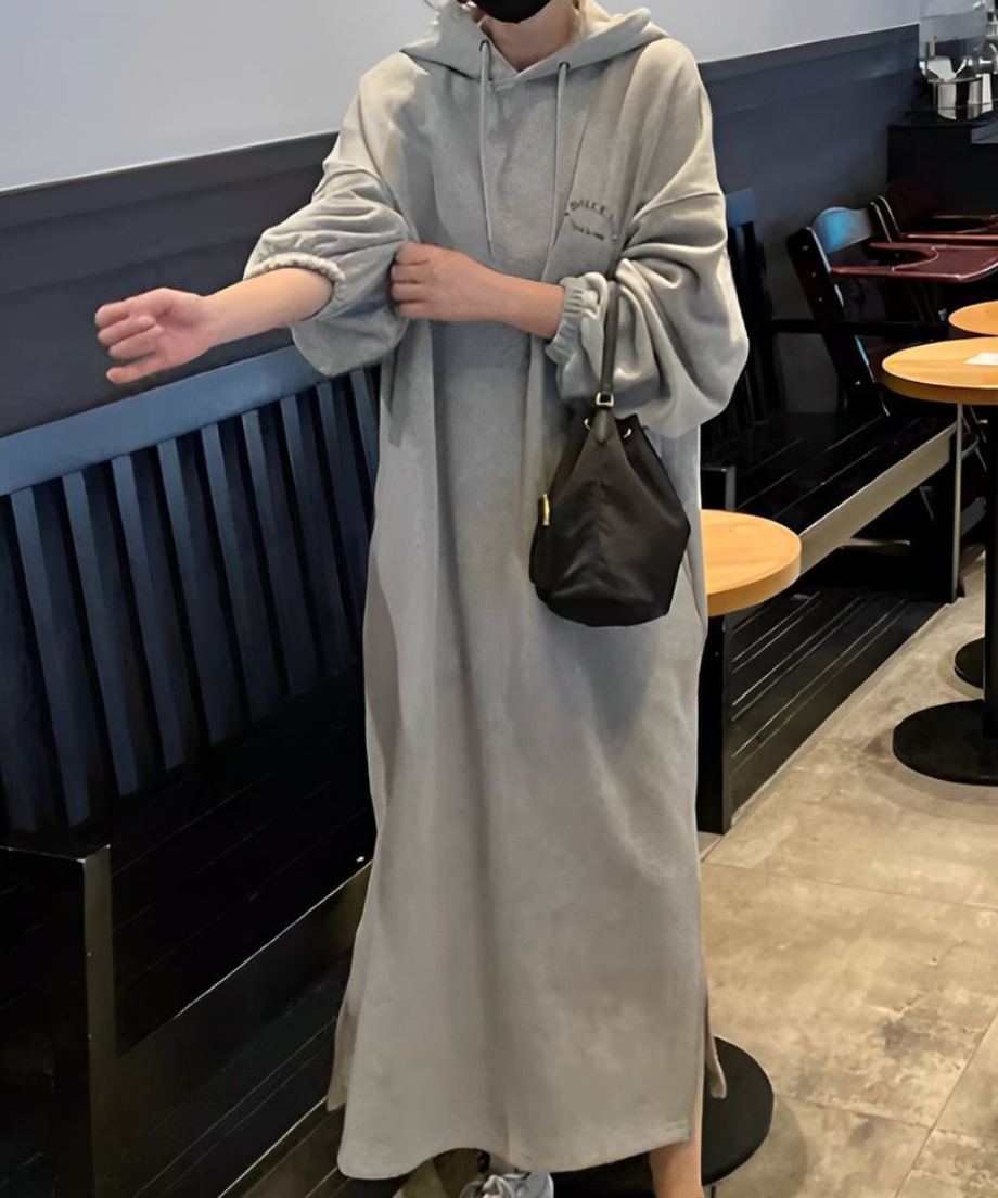 ロング丈フーディワンピースを着た女性が黒い巾着バッグを右手に持ち、オーバーサイズのゆったりとしたシルエットが特徴