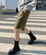 オリーブのハーフパンツに黒の厚底サイドゴアブーツを合わせ、横断歩道を歩くアクティブなデイリールック。