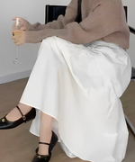 白いティアード切り替えマキシスカートを履いた女性が、ベージュの長袖ニットを着用し、座っている写真。

