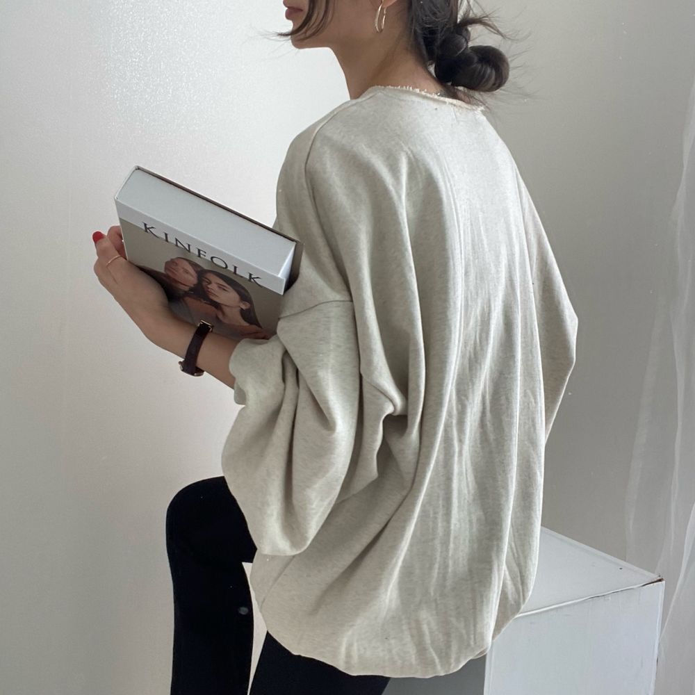 グレーのオーバーサイズプルオーバーを着用し、後ろを向いている女性のバストアップ。黒いレギンスに、切りっぱなしの襟元が見えるラフな着こなし。