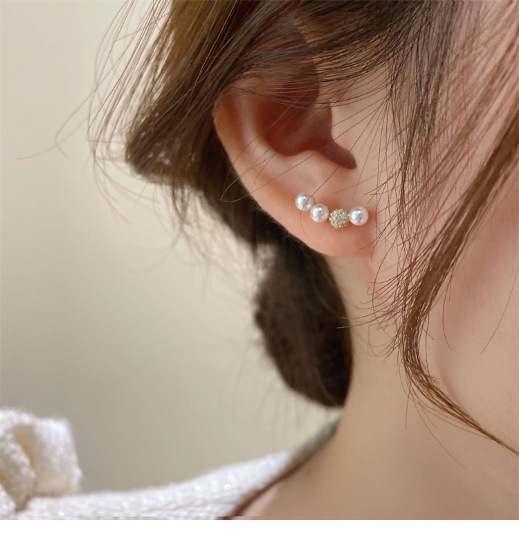 女性の耳に着用された、パール3粒と中央のラインストーンが連なるゴールドのラインピアス。耳たぶに沿ってカーブしているデザイン。