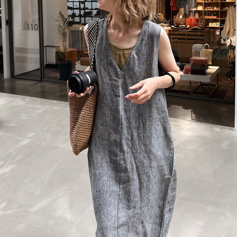 グレーのリネンノースリーブワンピースを着た女性がコーヒーを持っている