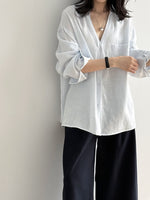 ライトブルーのVネックブラウスを着た女性。Vネックとゆったりとしたシルエットが特徴。