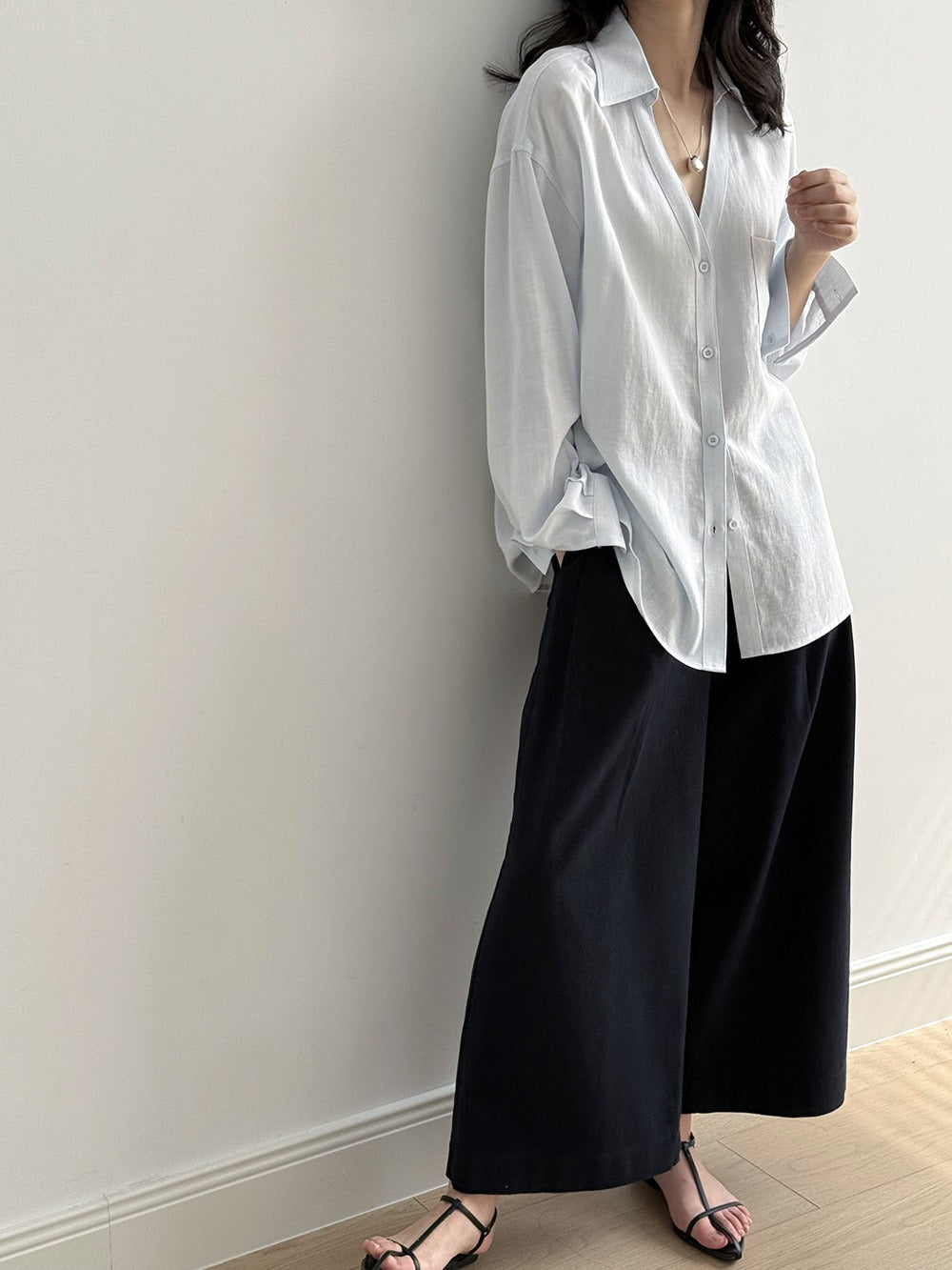 ライトブルーのVネックブラウスを着た女性。Vネックとゆったりとしたシルエットが特徴。