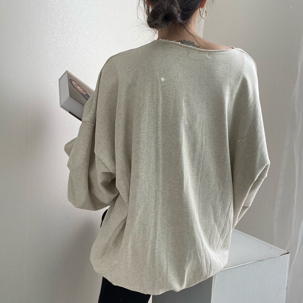グレーのオーバーサイズプルオーバーを着用し、後ろを向いている女性のバストアップ。切りっぱなしの襟元が見えるラフな着こなし。