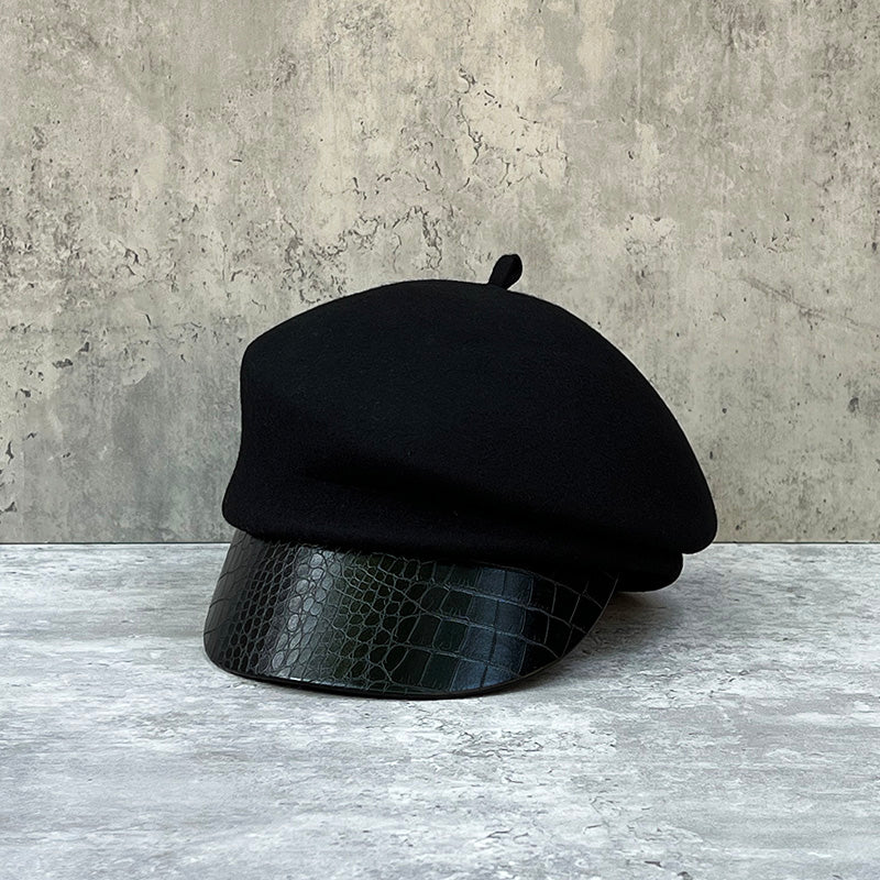 グレーの背景の上に、本体がブラックのウール調素材、ツバが黒のクロコダイル型押しレザーのキャップが正面から置かれている。