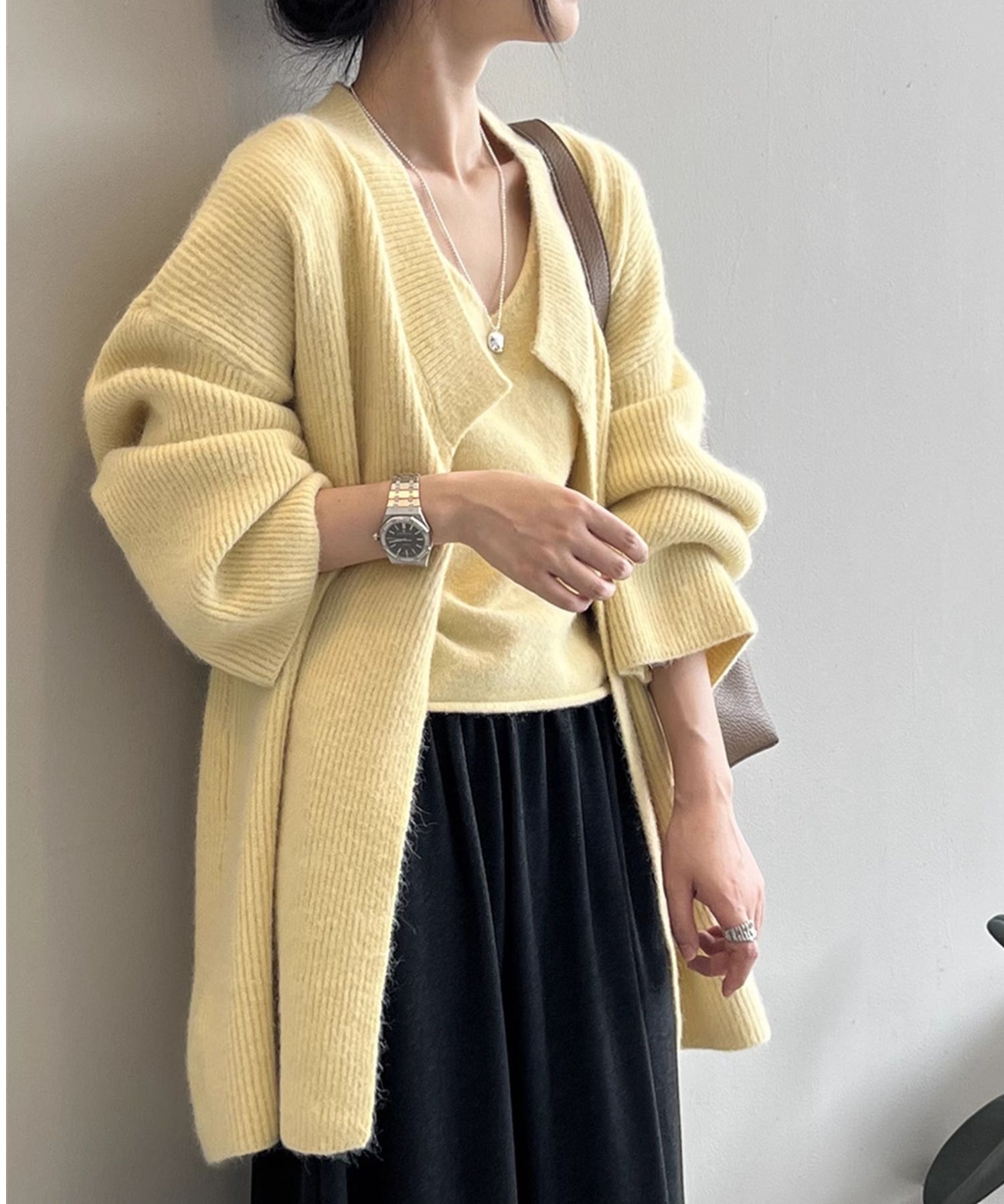 クリームイエローのVネックニットアンサンブルを着用し、茶色のバッグと時計をした女性のコーディネート。