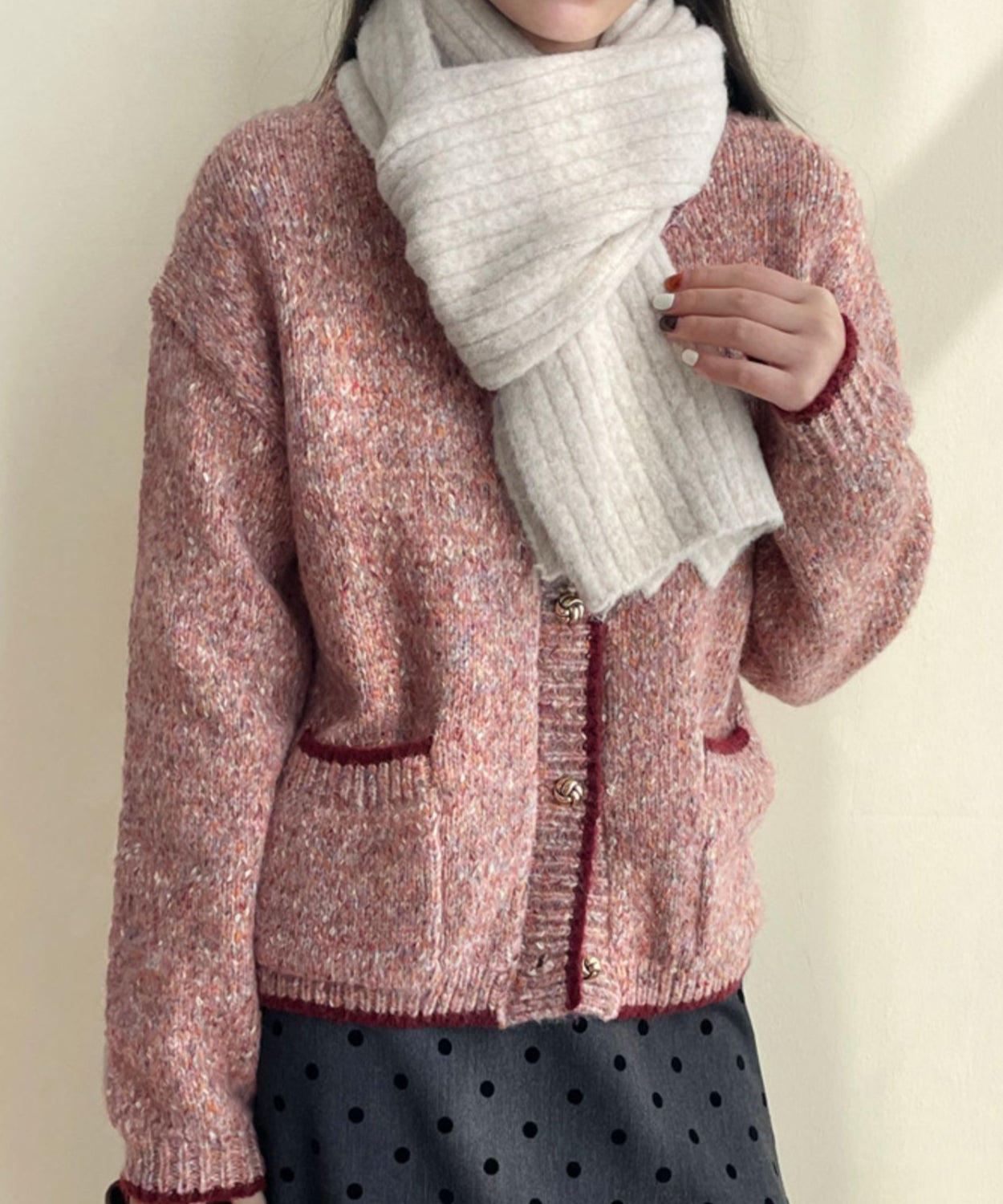 ローズピンクのカーディガンを着用し、ベージュのマフラーを巻いた女性のバストアップ。ドット柄のボトムスと合わせた秋冬コーディネート。