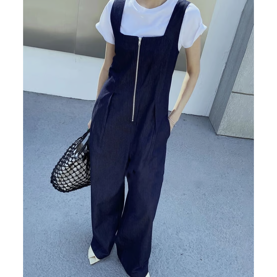 白Tシャツの上にデニムオールインワンを重ね着し、網バッグを持って立っている女性のクローズアップ写真。