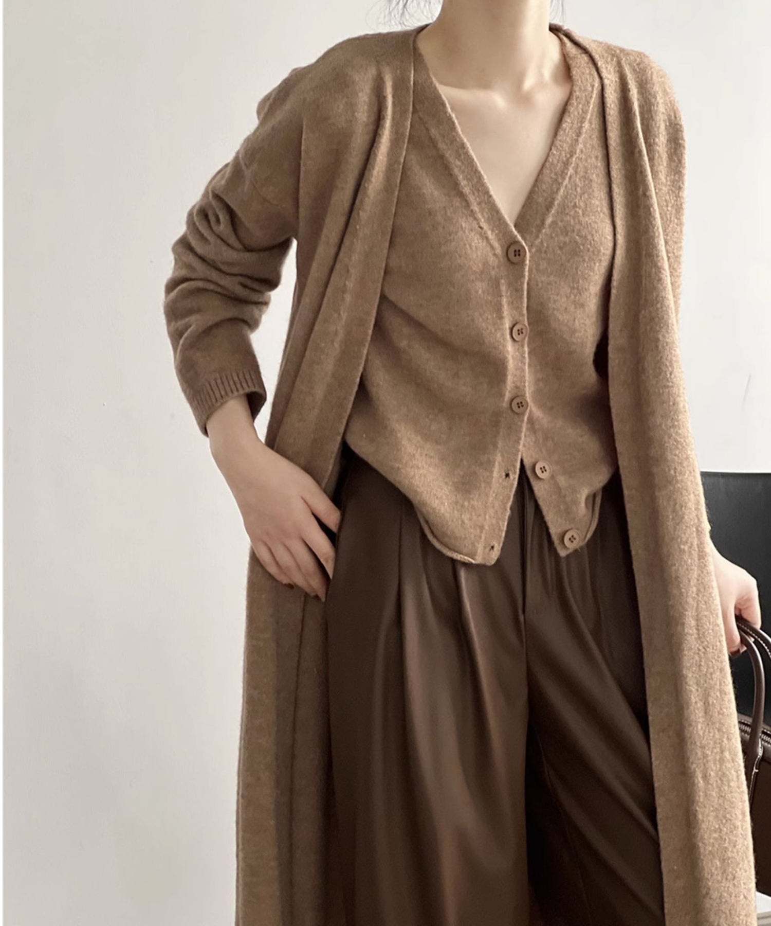 キャメルのロングカーディガンとベストを重ね着し、茶系のワイドパンツと合わせたシックな装いの女性。