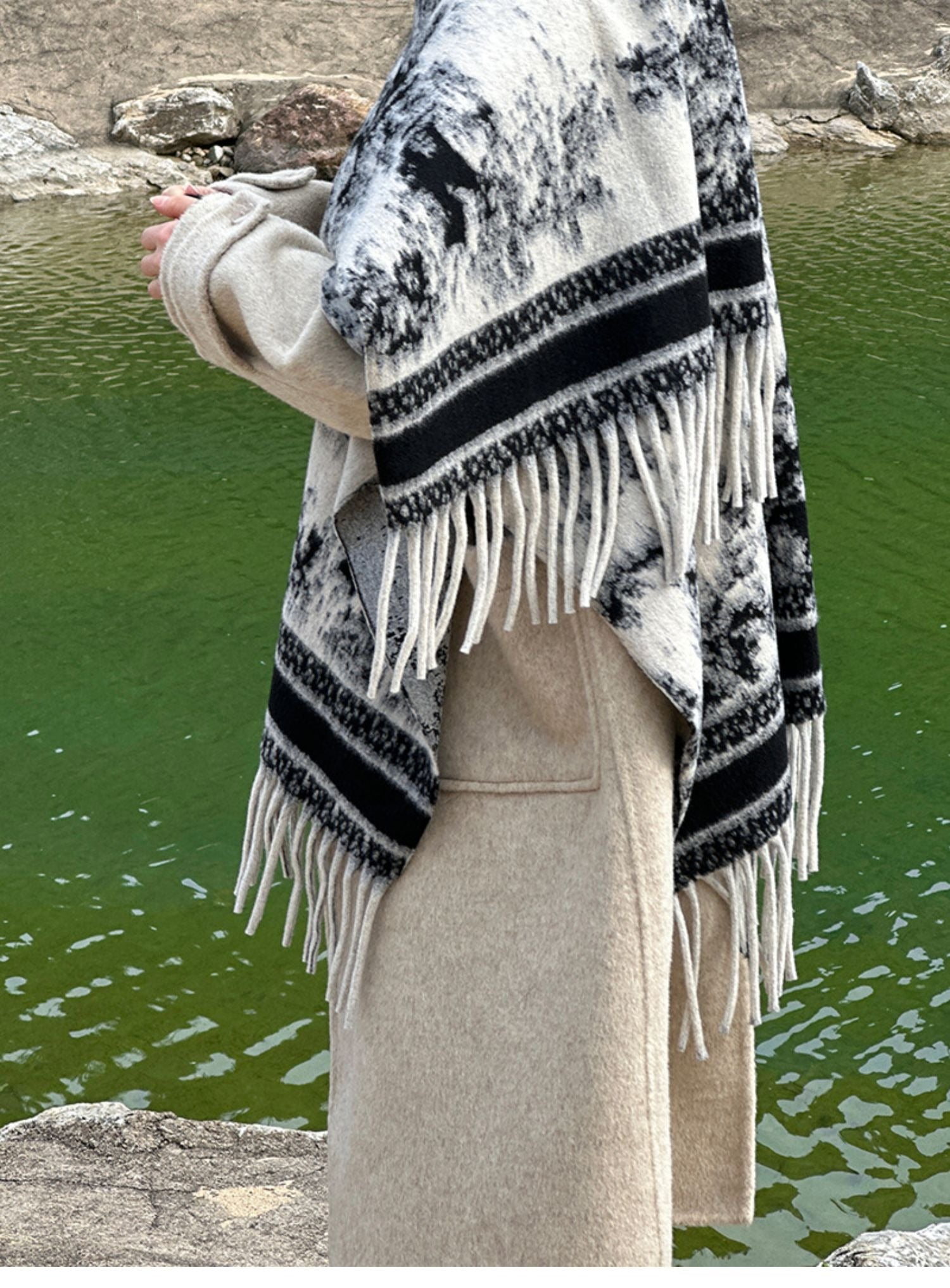 モノトーンの水墨画風の柄ショールをベージュのコートと合わせて屋外で着用する女性の横からのスタイル。