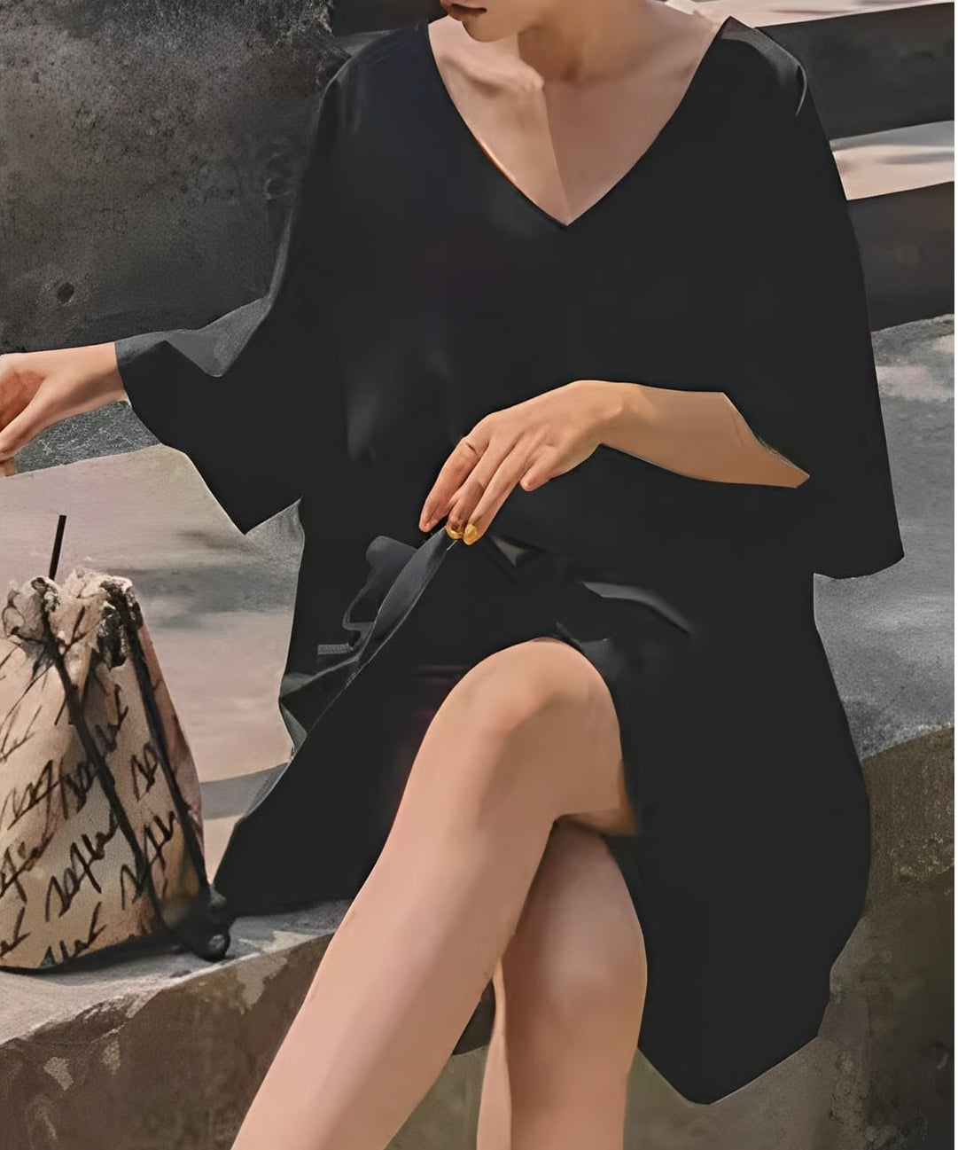 黒のVネックドルマンチュニックを着用し、ベンチに座ってポーズをとる女性のショット。
