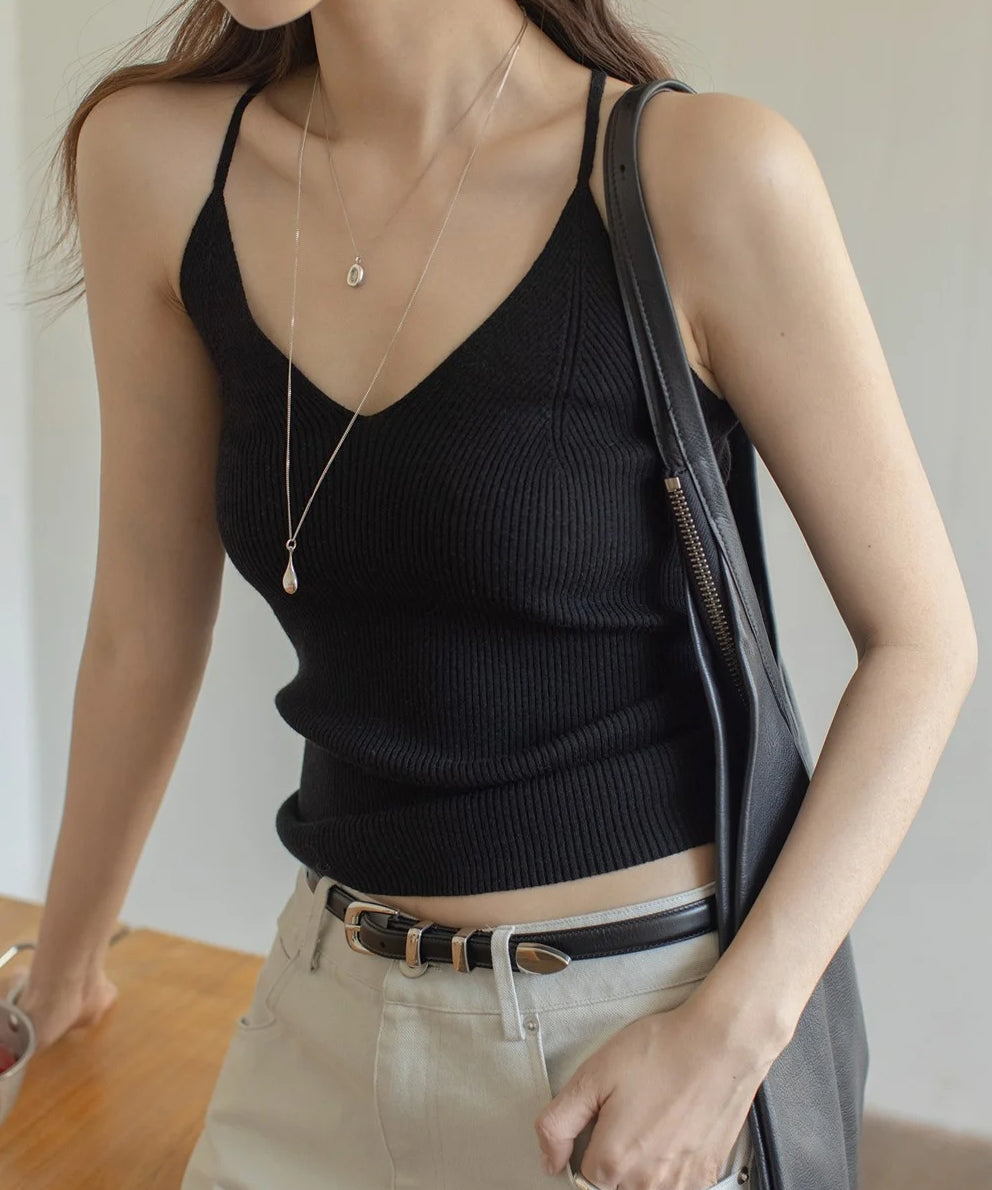 黒のリブ編みVネックキャミソールを着用した女性の半身。ライトベージュのパンツと黒いベルト、黒のバッグを肩にかけてシルバーのネックレスを着用。