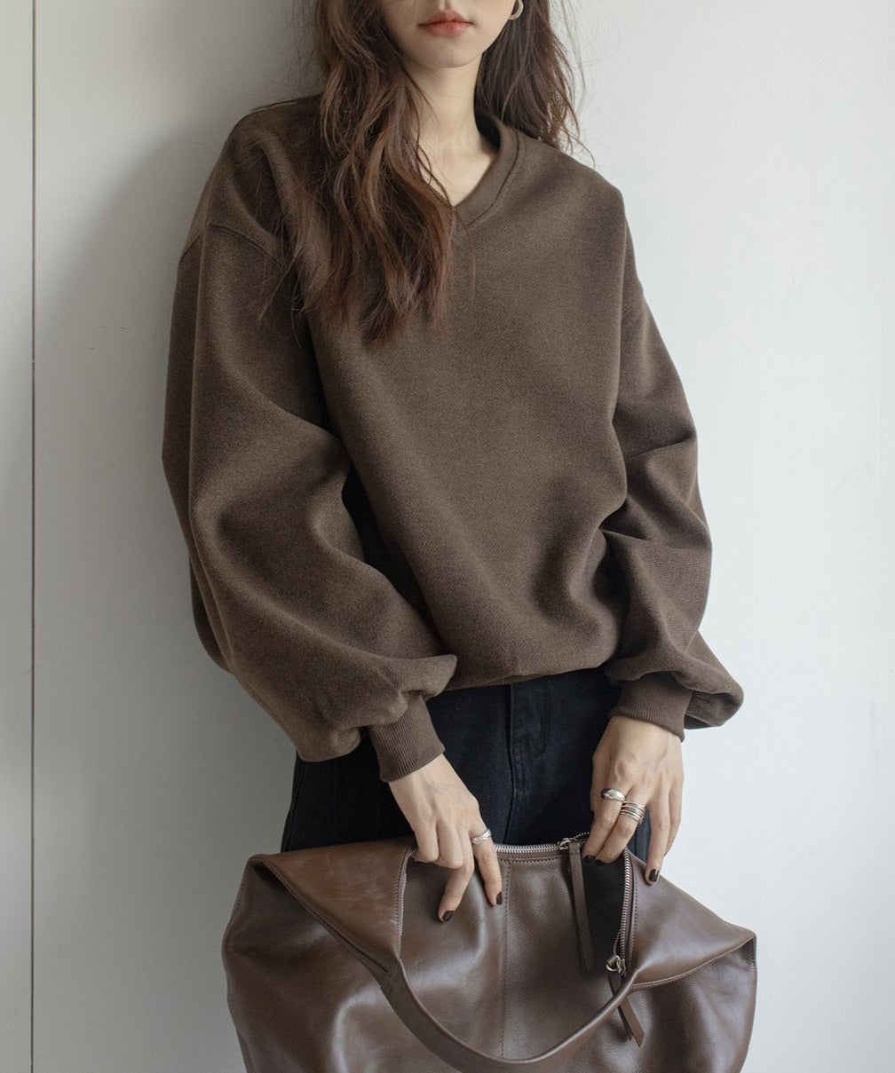 ブラウンのVネックバルーンスリーブトップスを着た女性のクローズアップ。茶色の大きなバッグを持っている。