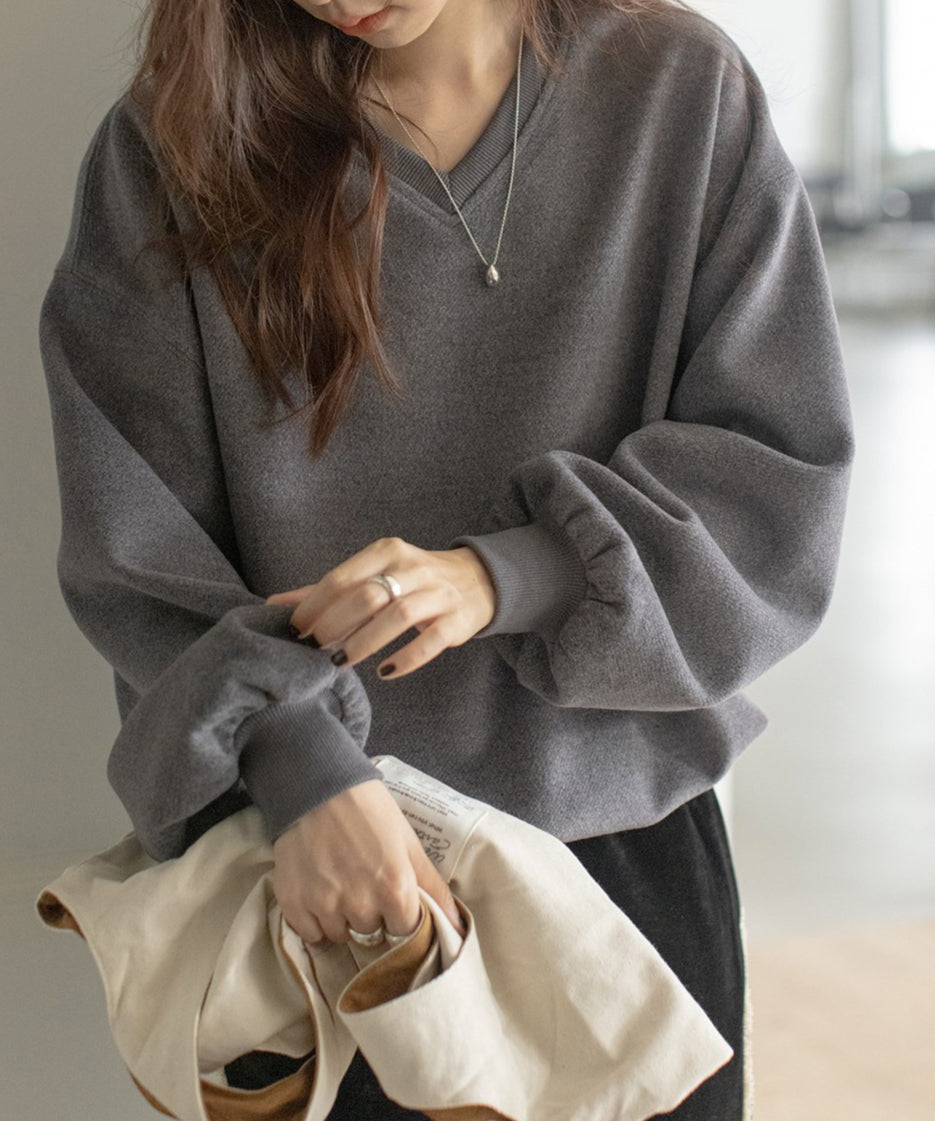 グレーのVネックバルーンスリーブトップスと黒のベロアワイドパンツを合わせた女性。袖部分のクローズアップ。