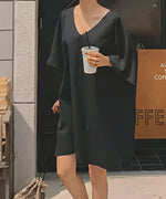 黒のVネックドルマンチュニックを着用し、ドリンクを持って屋外に立つ女性の全身コーディネート。