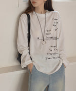 白のメッセージプリントロングTシャツとライトブルーのワイドデニムパンツを着用した女性の全身。黒いバッグを肩から下げている。