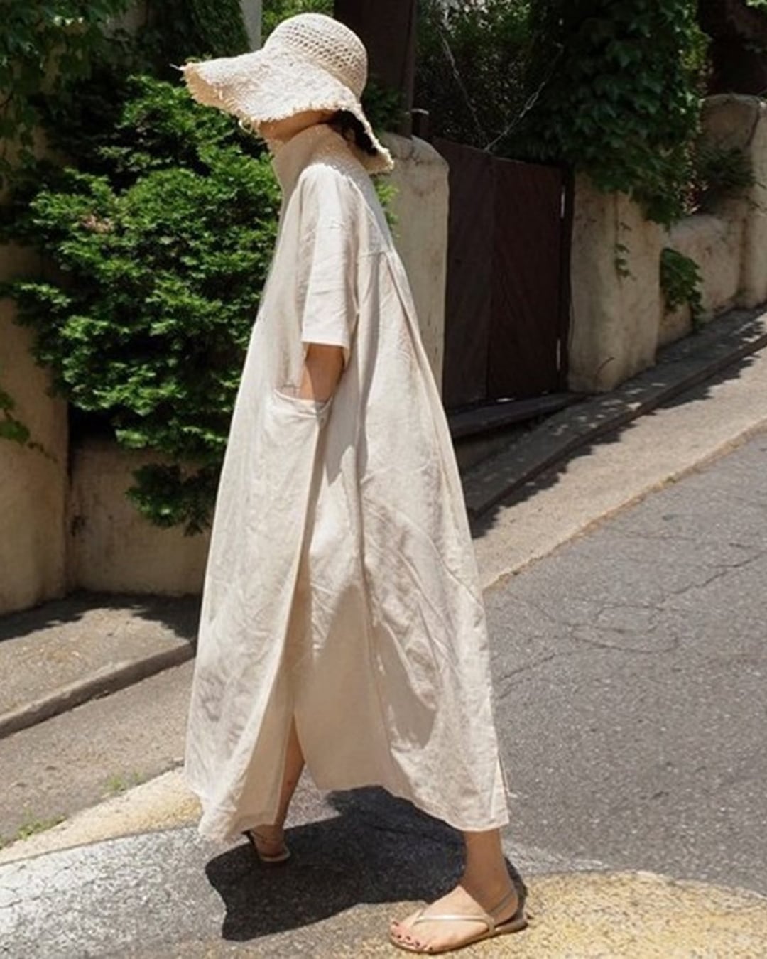 ベージュのリネンドレスを着た人物が屋外を歩いている写真。ゆったりとしたシルエットと軽やかな素材感が特徴。