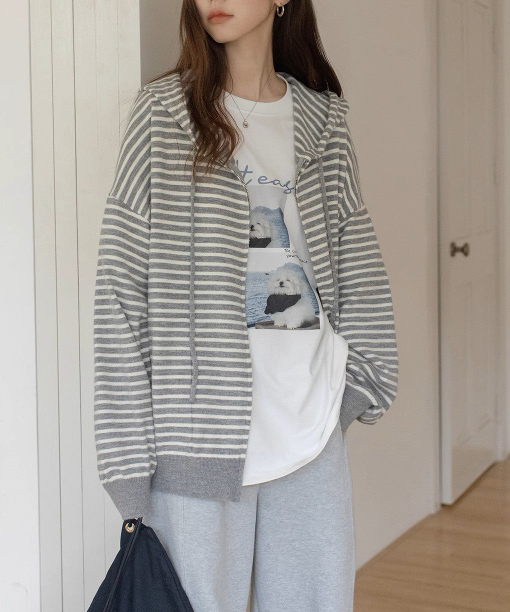 グレーと白の細いボーダー柄のジップアップパーカーを着用した女性の半身。インナーには白いTシャツ、ボトムスにはライトグレーのスウェットパンツを合わせたカジュアルな着こなし。