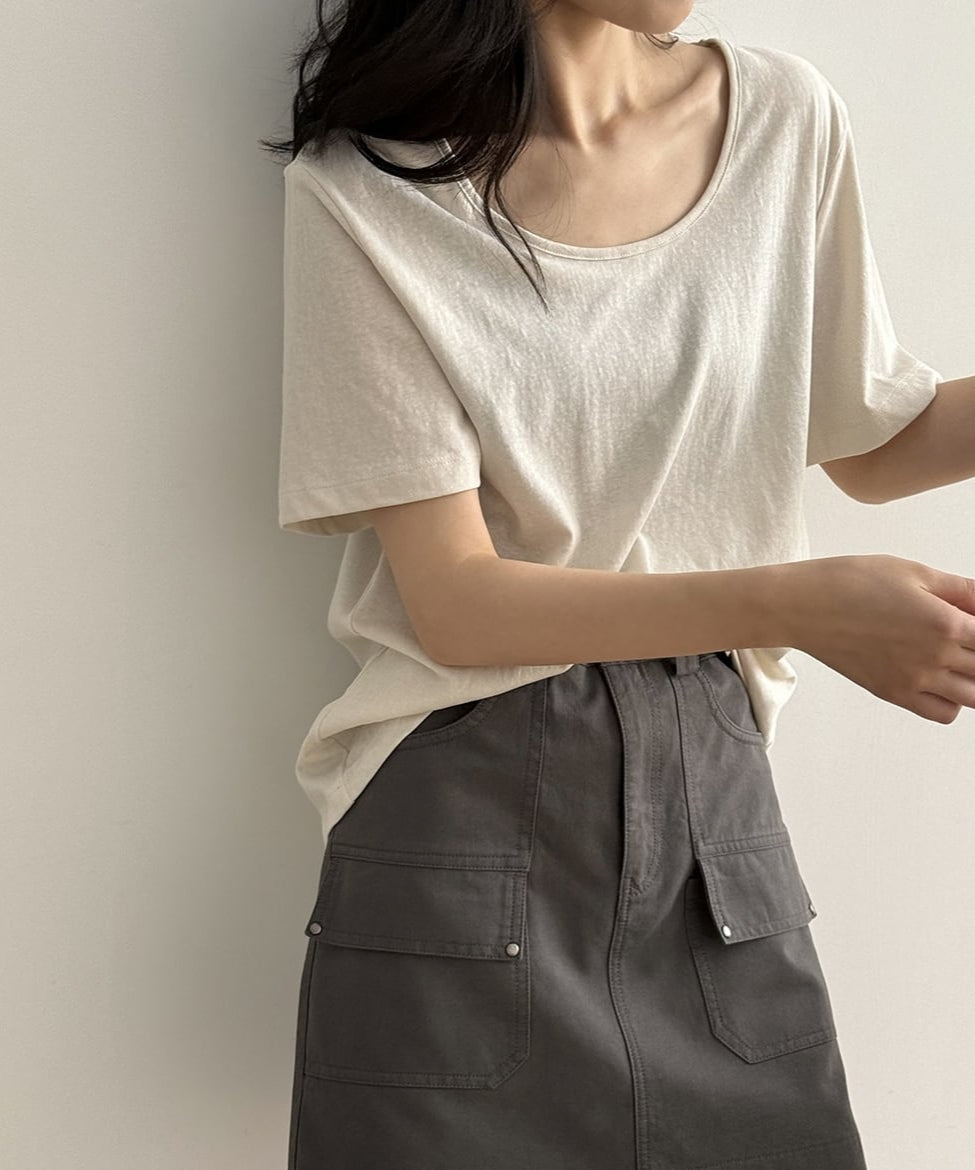 アプリコットのUネックTシャツを着用した女性の上半身。Tシャツをグレーのカーゴポケット付きミニスカートに軽くタックインしている。