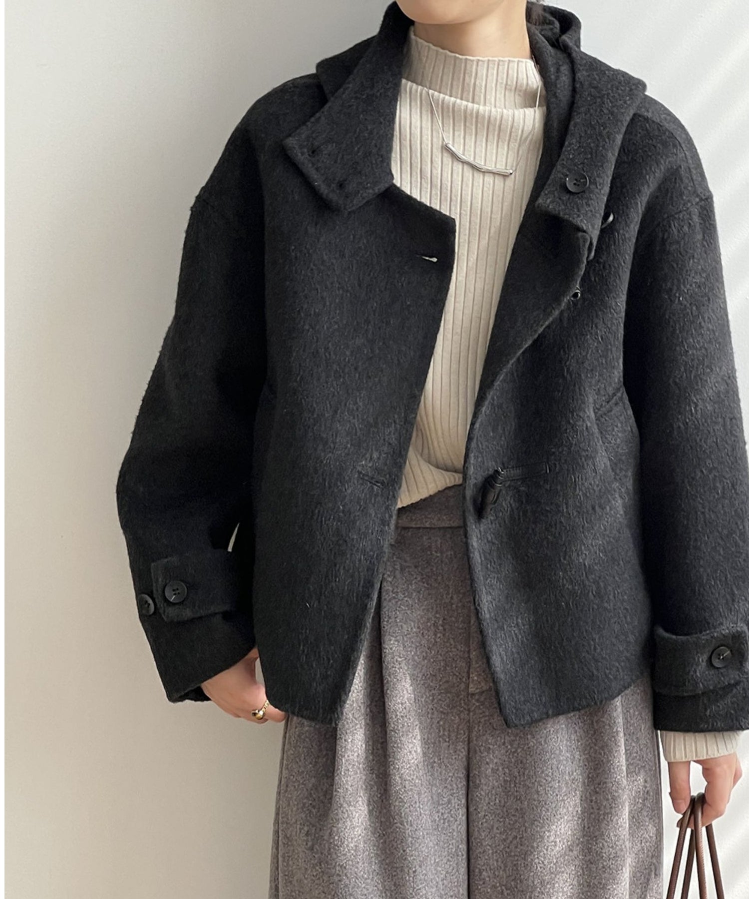 黒のショート丈ジャケットを着用した女性。インナーは白のリブニット、ボトムスはグレーのワイドパンツを合わせたきれいめカジュアルなコーディネート。