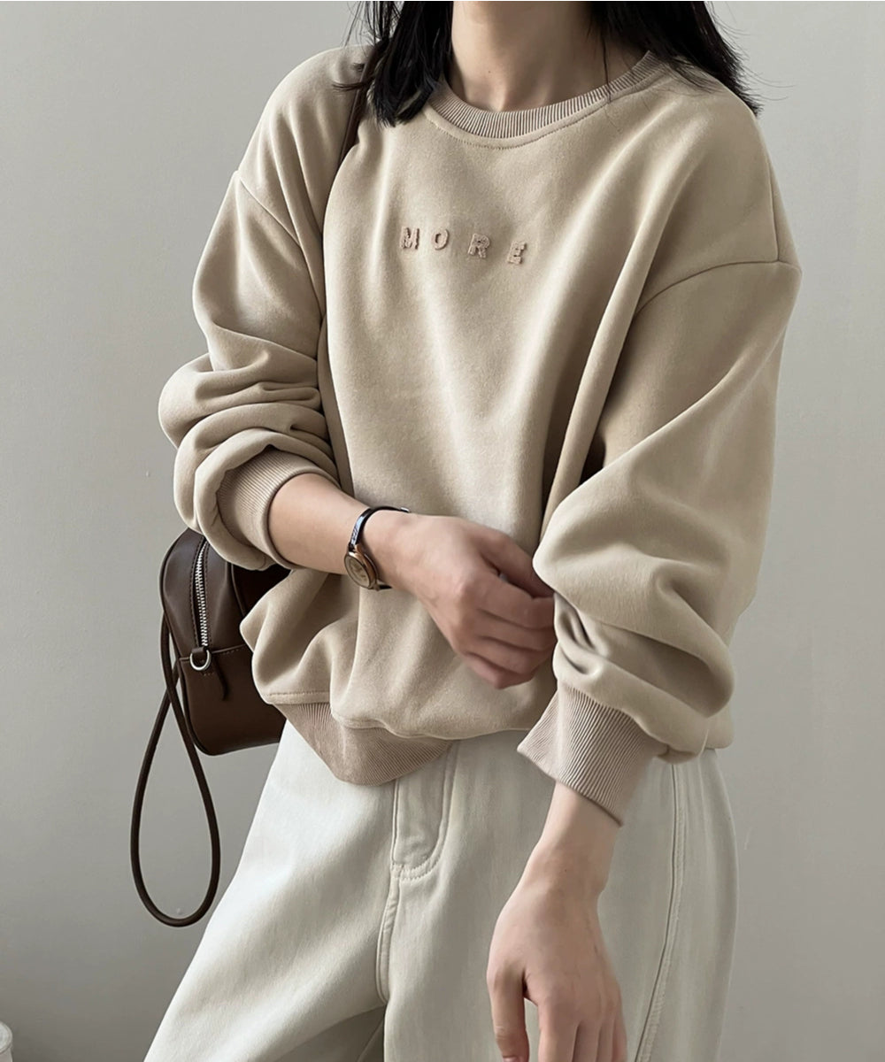 アプリコットのスウェットシャツの袖をまくった女性が茶色のバッグを持っている。