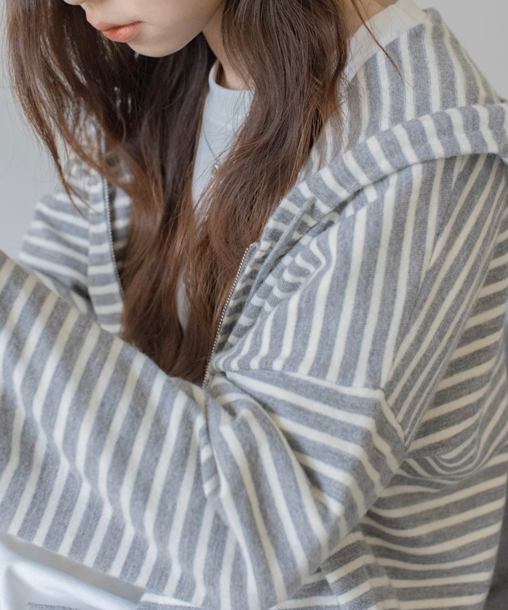 グレーと白の細いボーダー柄のジップアップパーカーを着用した女性の接写ショット。ラグランスリーブの袖の様子が見える