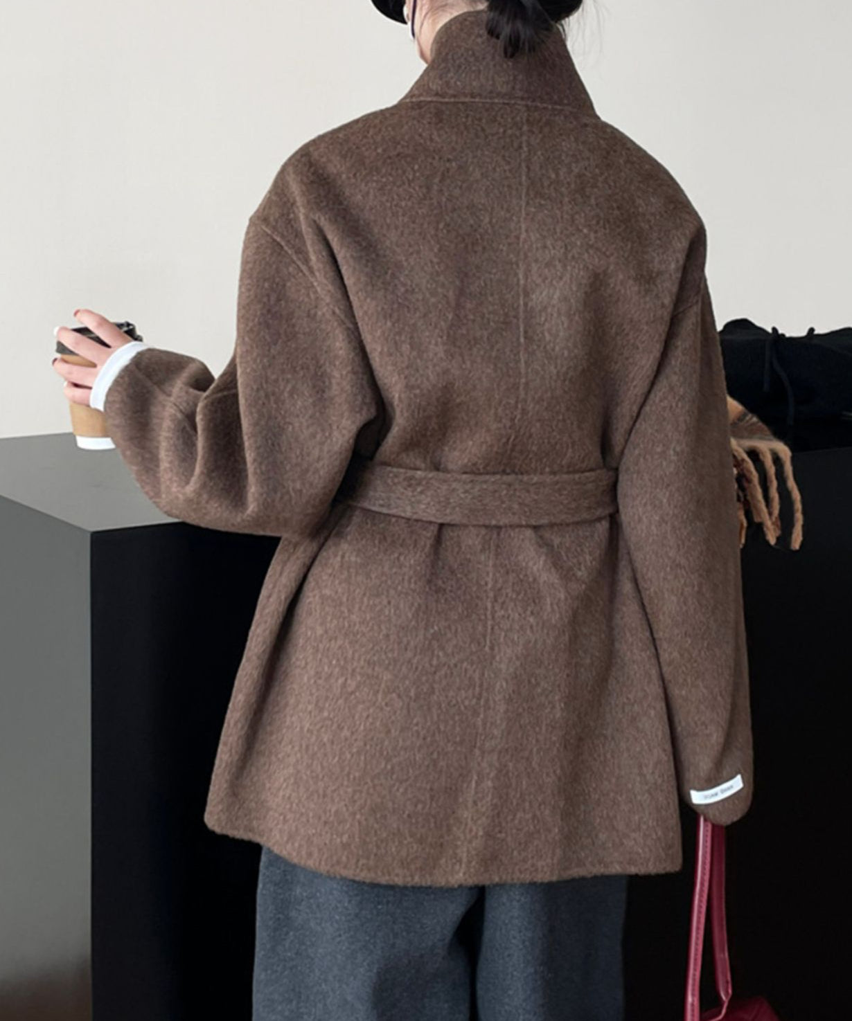 ブラウンのスタンドカラーコートを着用し、赤いバッグを持った女性の後ろ姿。