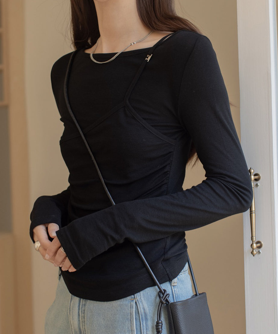 ブラックのレイヤードデザインのロングスリーブトップスを着用した女性の半身。トップスは胸元にキャミソールが重ねられたようなデザインで、黒のミニバッグを斜めがけし、シルバーのネックレスを着用。