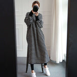 白黒ボーダー柄のロングワンピースを着て、白いスニーカーを履いた女性が、カメラで自身の姿を鏡越しに撮影している側面の立ち姿。