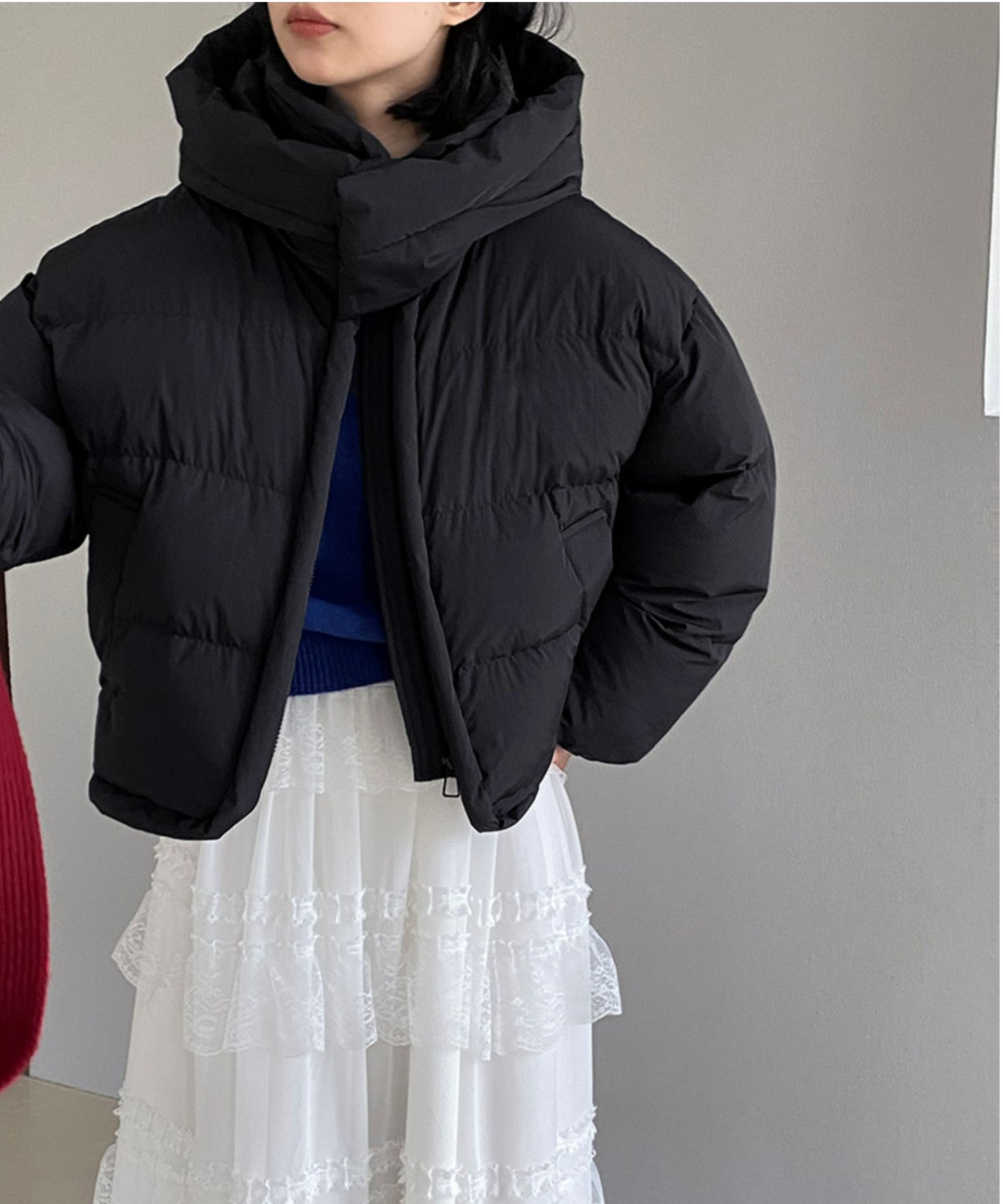 黒のショート丈パディングジャケットを着用した女性の半身。白のレーススカートを合わせた冬のコーディネート。ボリュームのある襟元が特徴。