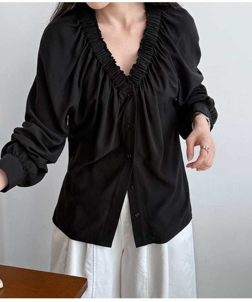 黒いVネックギャザーブラウスに白いワイドパンツを合わせた女性のコーディネート。