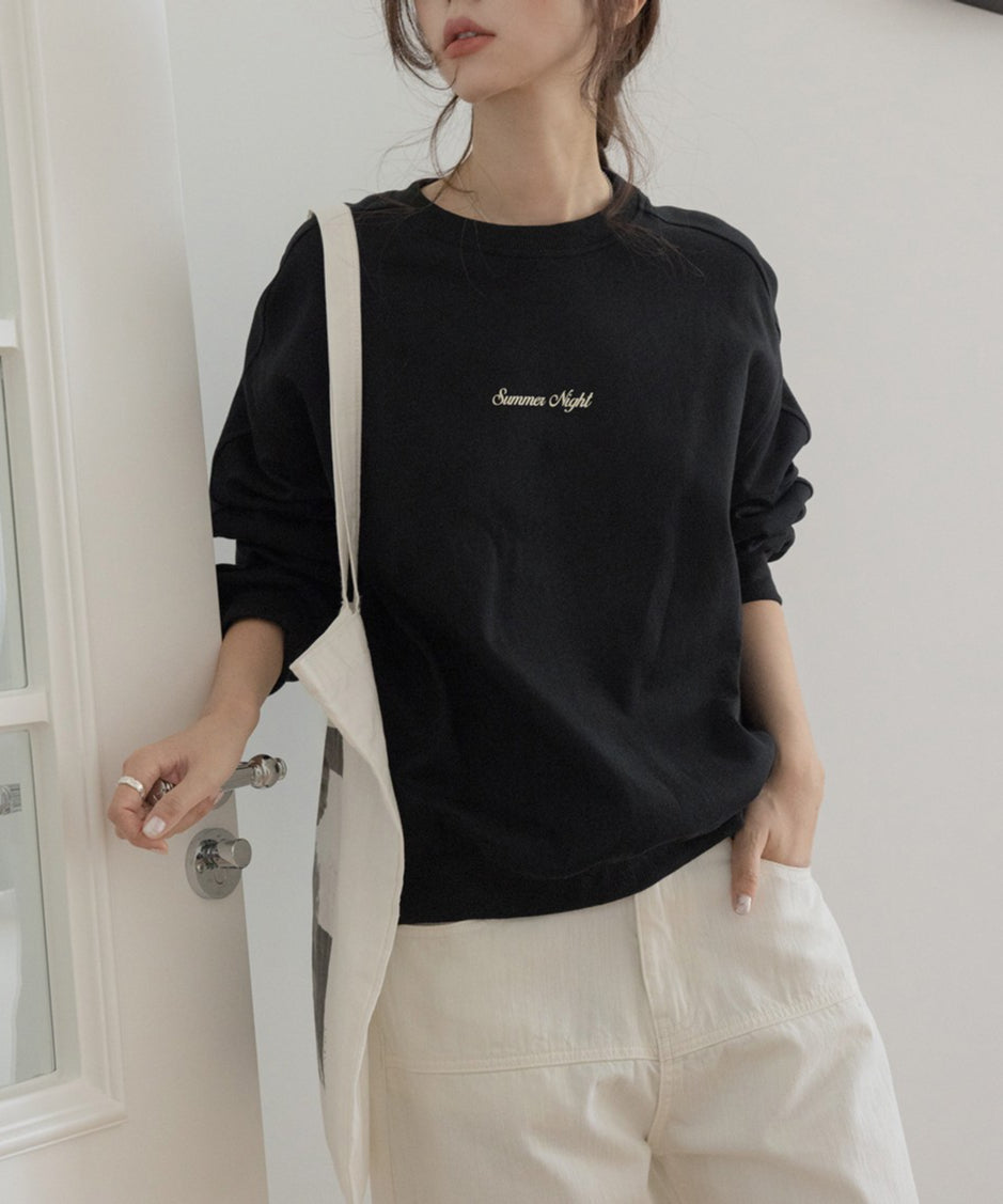 黒のオーバーサイズスウェットを着用し、白のボトムスを着用した女性。「Summer Night」の刺繍ロゴがある。