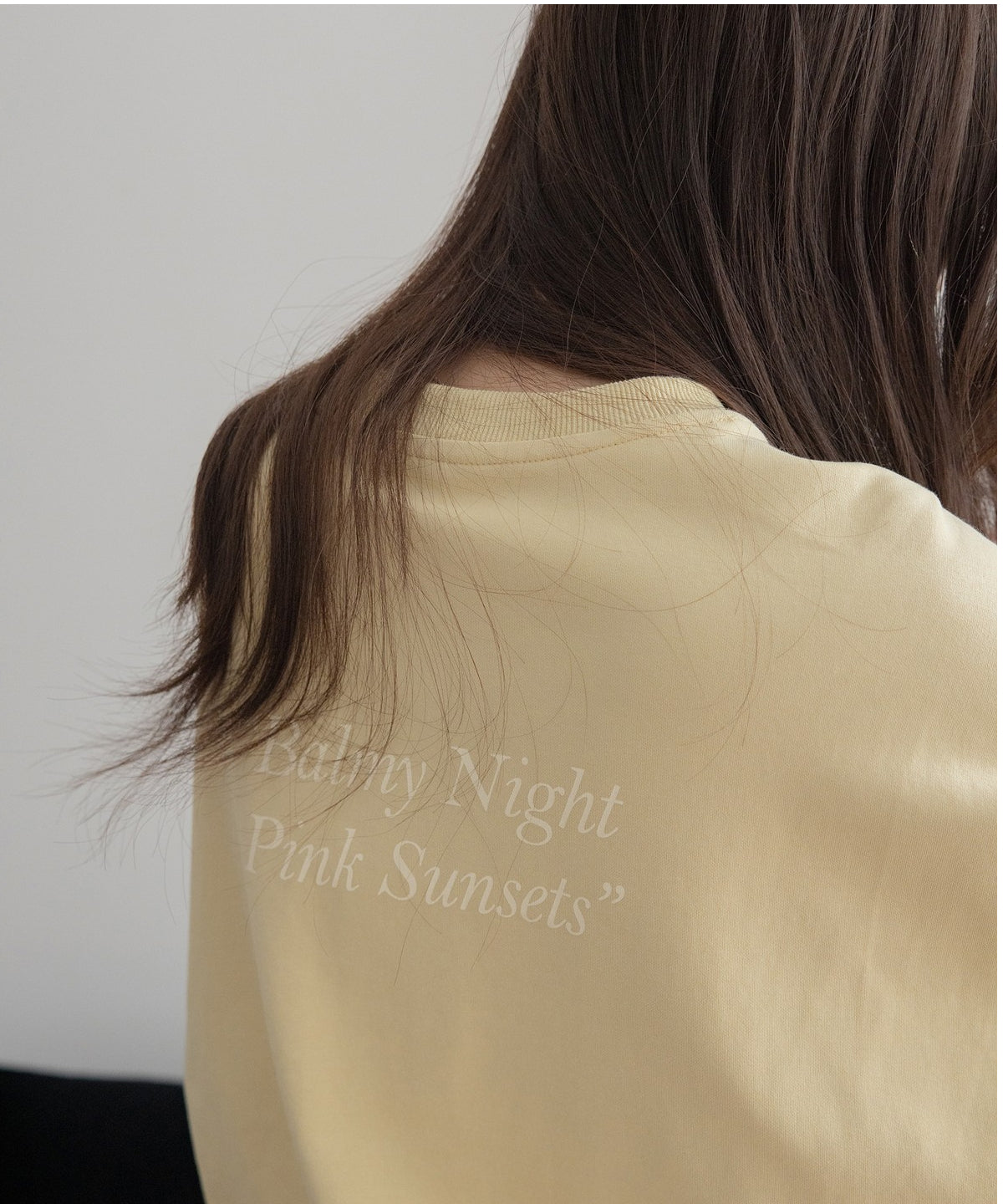 ライトイエローのオーバーサイズスウェットの背面クローズアップ。背中には「Balmy Night Pink Sunsets」の薄い白色のプリントが施されている。