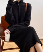 黒のハーフジップリブニットロングワンピースを着用し、椅子に座って白いカップを持つ女性の画像。