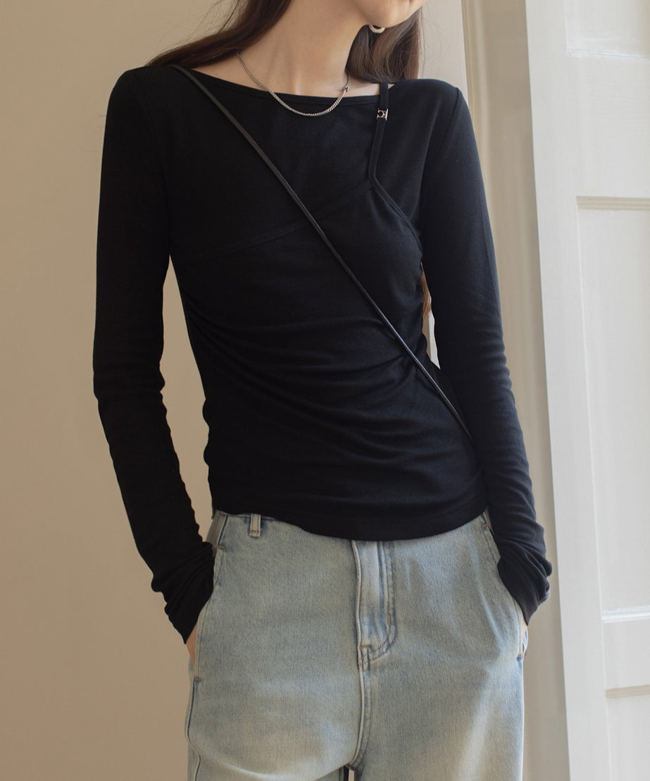 ブラックのレイヤードデザインのロングスリーブトップスを着用し、シルバーのネックレスをつけた女性。ボトムスは薄いブルーのワイドデニムパンツ。