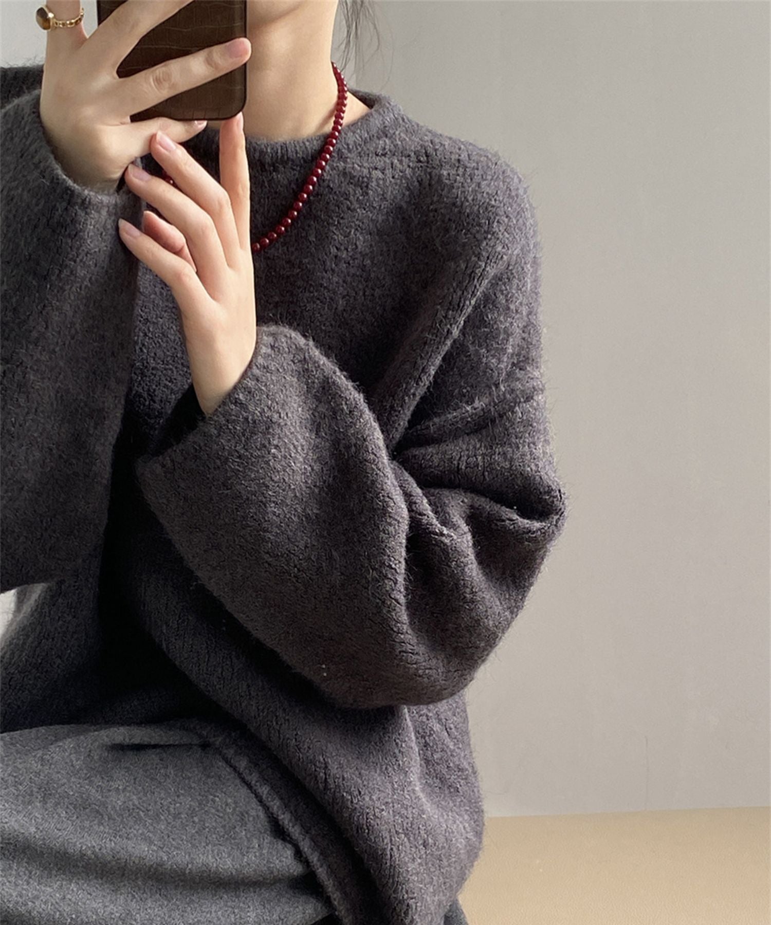 チャコールグレーのニットを着用した女性がスマホを手に持ち座っているショット。