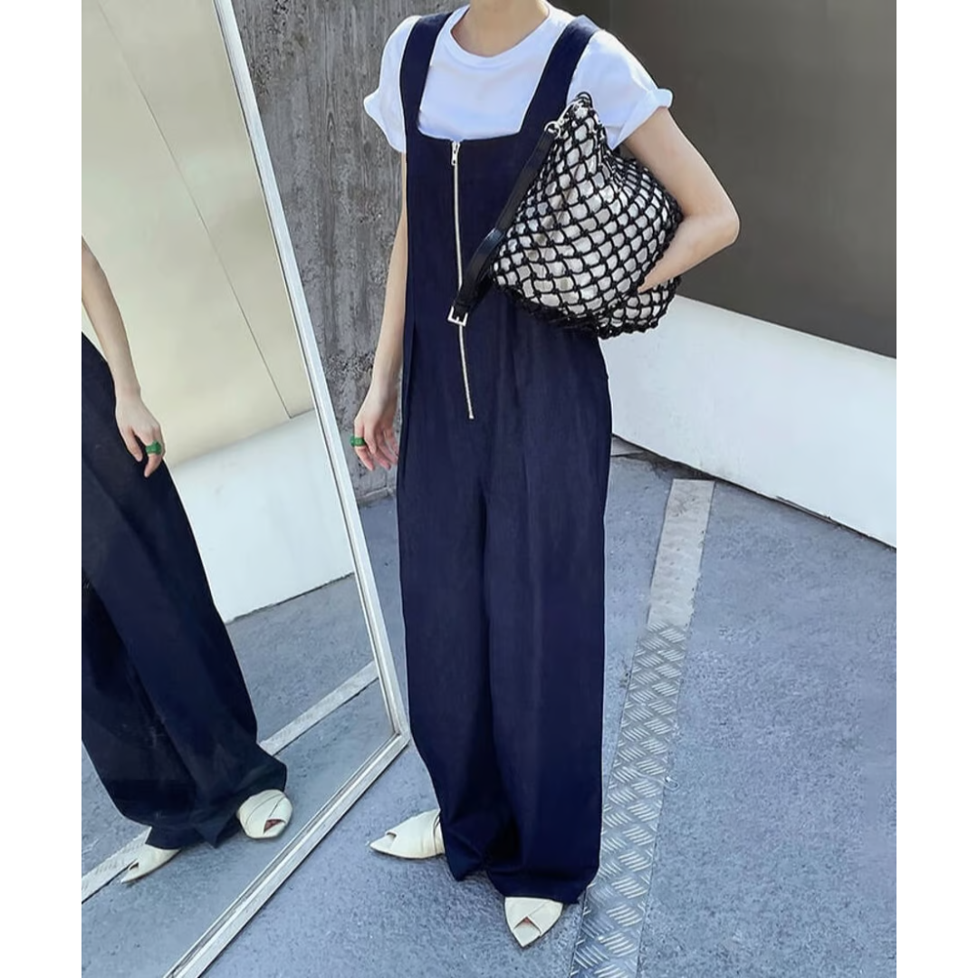 白Tシャツの上にデニムオールインワンを重ね着した女性の全身写真。鏡に映った姿も確認できる。