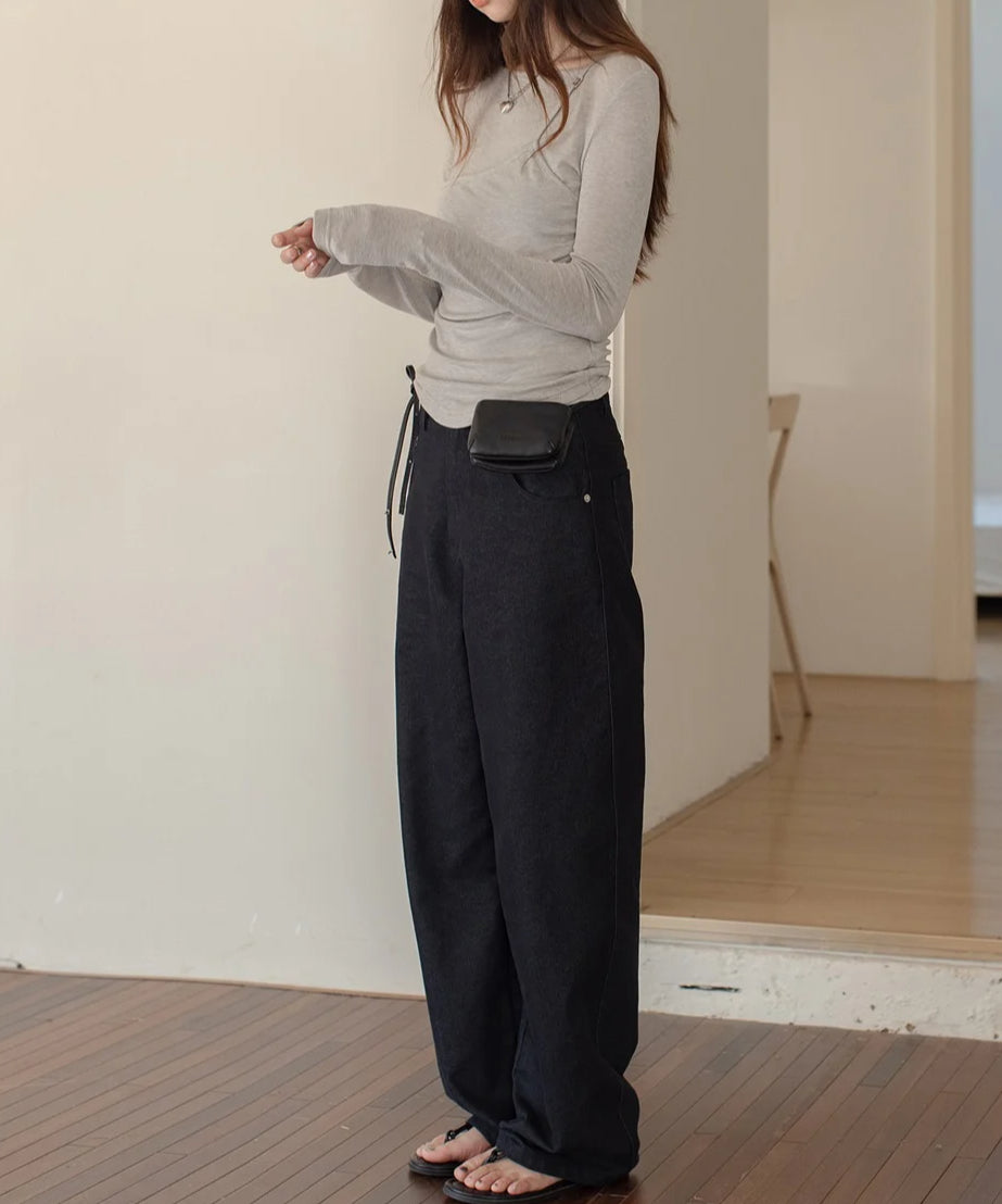 ライトグレーのレイヤードデザインのロングスリーブトップスを着用し、黒のボトムスを合わせた女性のクローズアップ。ドレープと袖口のサムホールが特徴的。