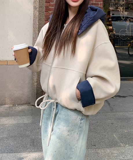 オフホワイトのオーバーサイズジャケットを着た女性が歩いている様子。フードと袖口はネイビーで、カジュアルなスタイル。
