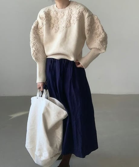 オフホワイトのフローラル刺繍セーターとネイビースカートを合わせ、大きな白いバックを持った全身コーディネート。