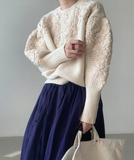 オフホワイトのフローラル刺繍セーターを着た女性、立体感のある編み込みの袖。