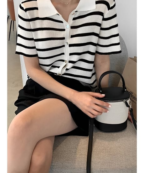 ボーダー柄のトップスと黒のボトムスを着た女性が、バイカラーのバニティバッグを横に置いている写真。