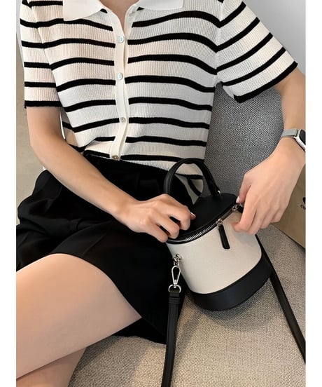 ボーダー柄のトップスと黒のボトムスを着た女性が、バイカラーのバニティバッグを膝上に置いているクローズアップ。