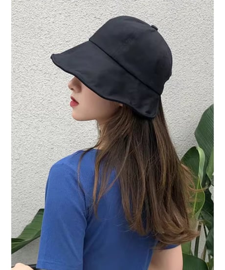 黒色のつば広キャップをかぶり、青いVネックのトップスを着た女性の後ろ姿。